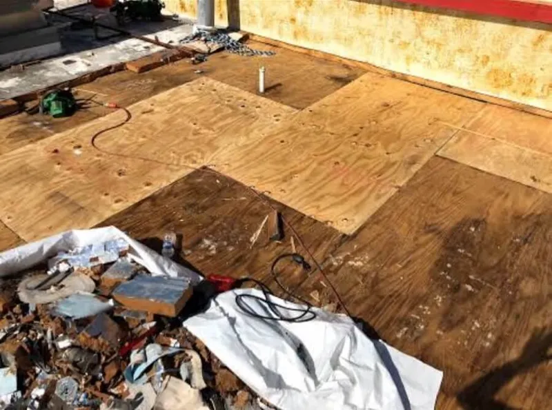 Workers removing damaged asphalt-saturated layers from a flat roof deck