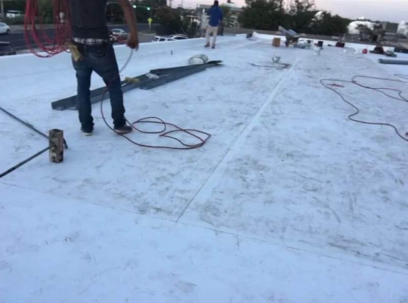 Heavy roll of white TPO membrane positioned on a commercial roof deck for installation